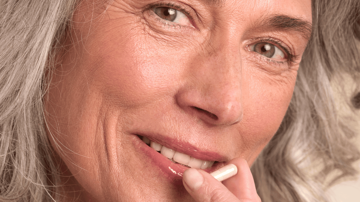Femme mature aux cheveux gris prenant un complément alimentaire de nutricosmétique.